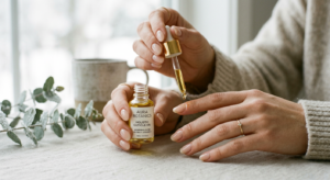 A close-up, editorial-style photograph of a woman’s well-manicured hands applying a golden, nourishi